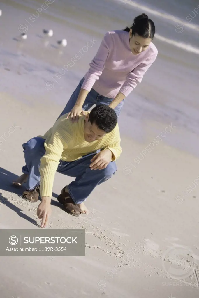 Young man writing in the sand with a young woman leaning on him
