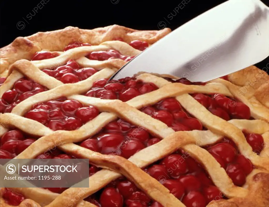 Close-up of a cherry pie being cut with a knife