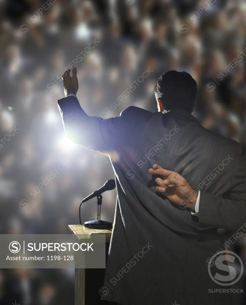 Rear view of a businessman talking at a podium with his fingers crossed behind his back