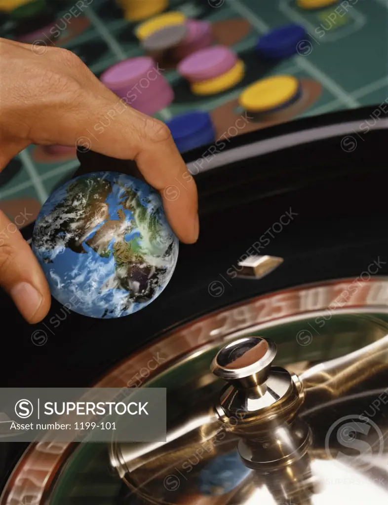 Close-up of a person's hand holding a globe over a roulette wheel