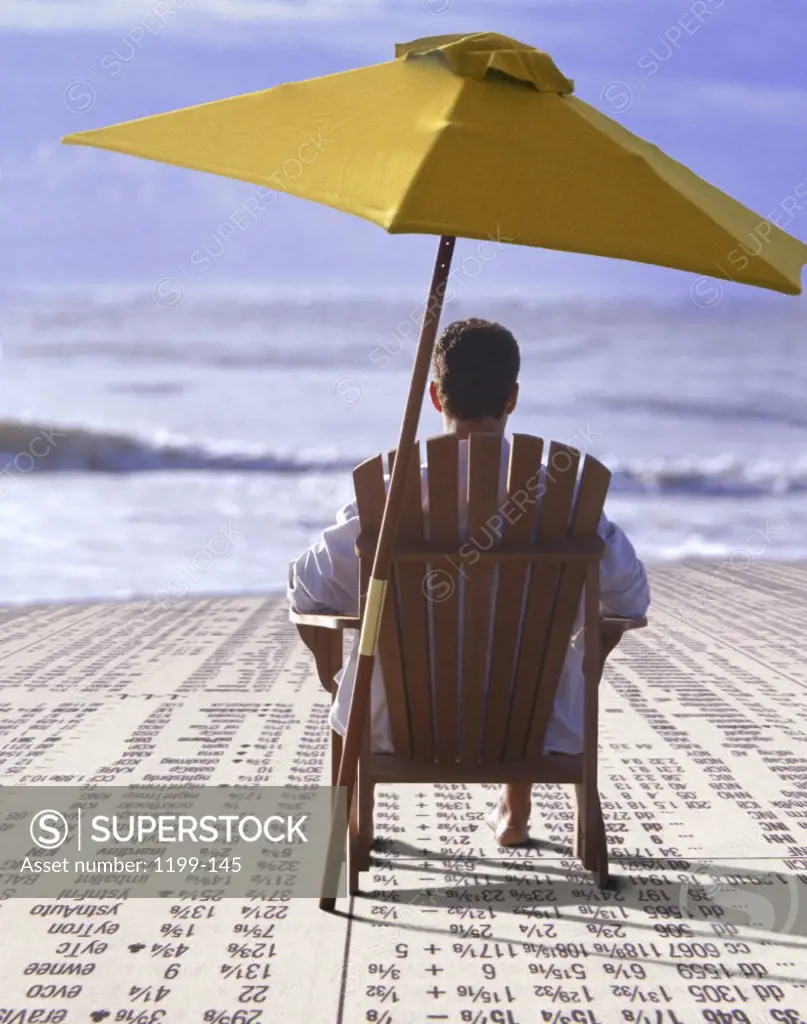 Rear view of a businessman sitting under a beach umbrella on the beach