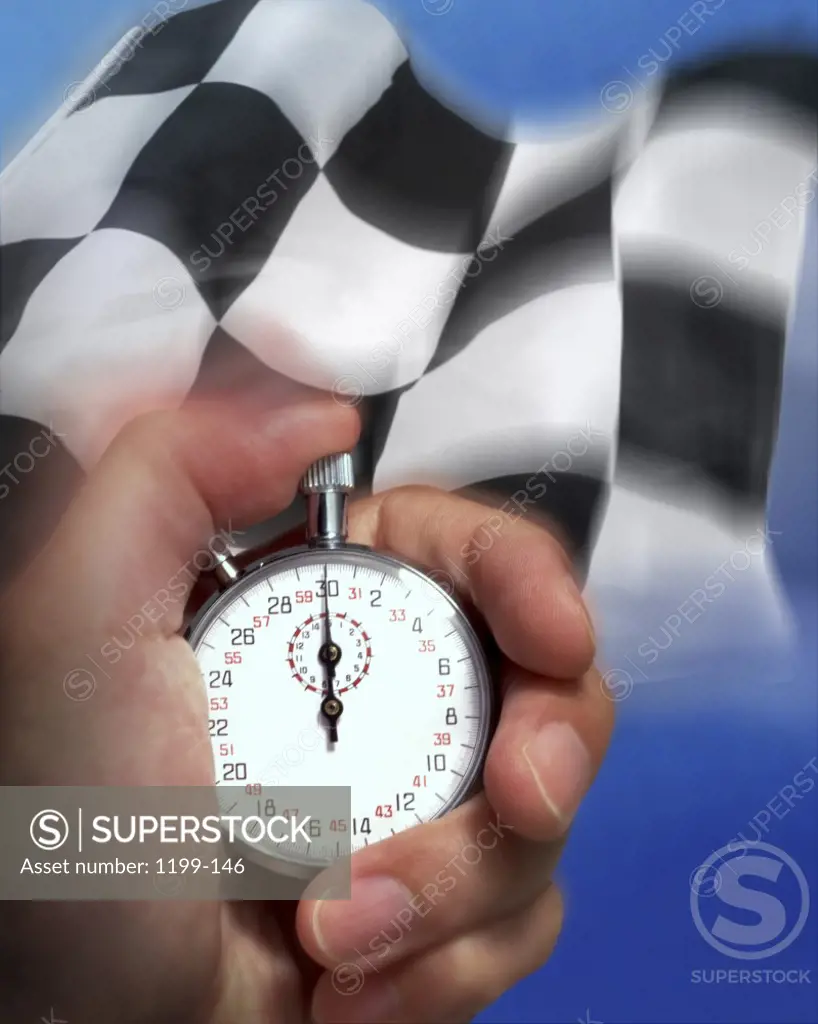 Person's hand holding a stopwatch in front of a checkered flag