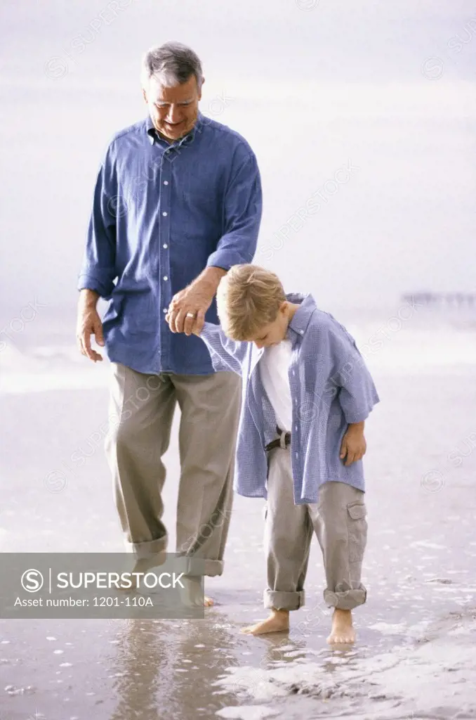 Grandfather and his grandson walking on the beach