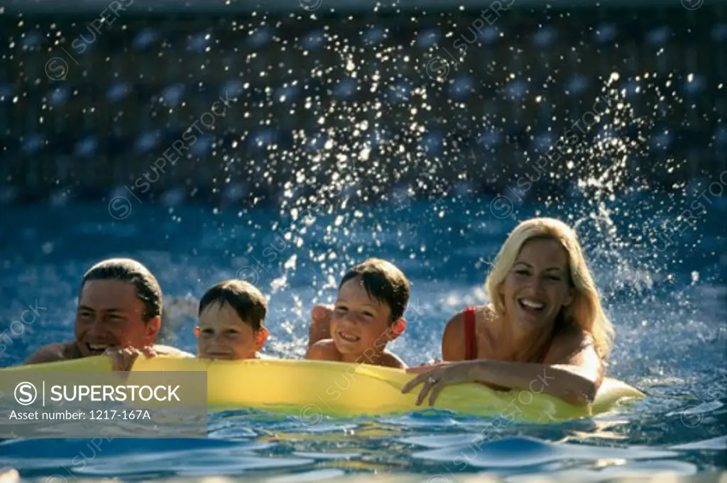 Mid adult couple with their two sons on a pool raft in a swimming pool