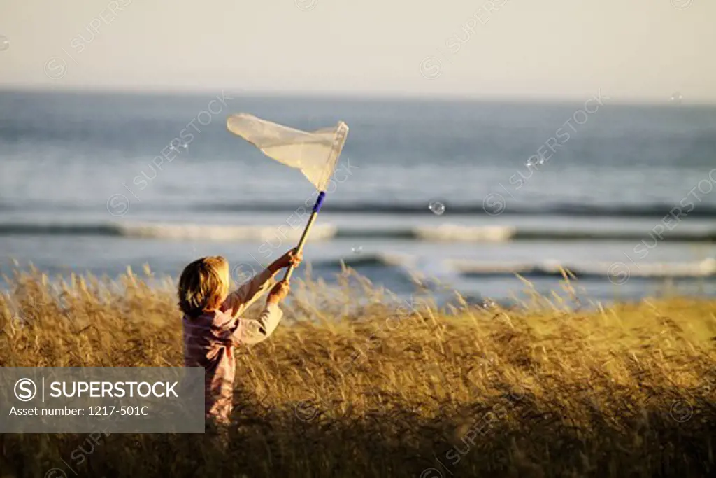 Boy trying to catch bubbles with a butterfly net in a field
