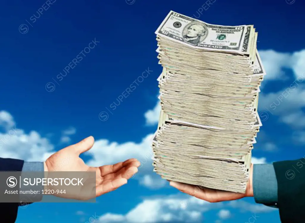 Close-up of a person's hand giving a stack of US dollar bills to another person