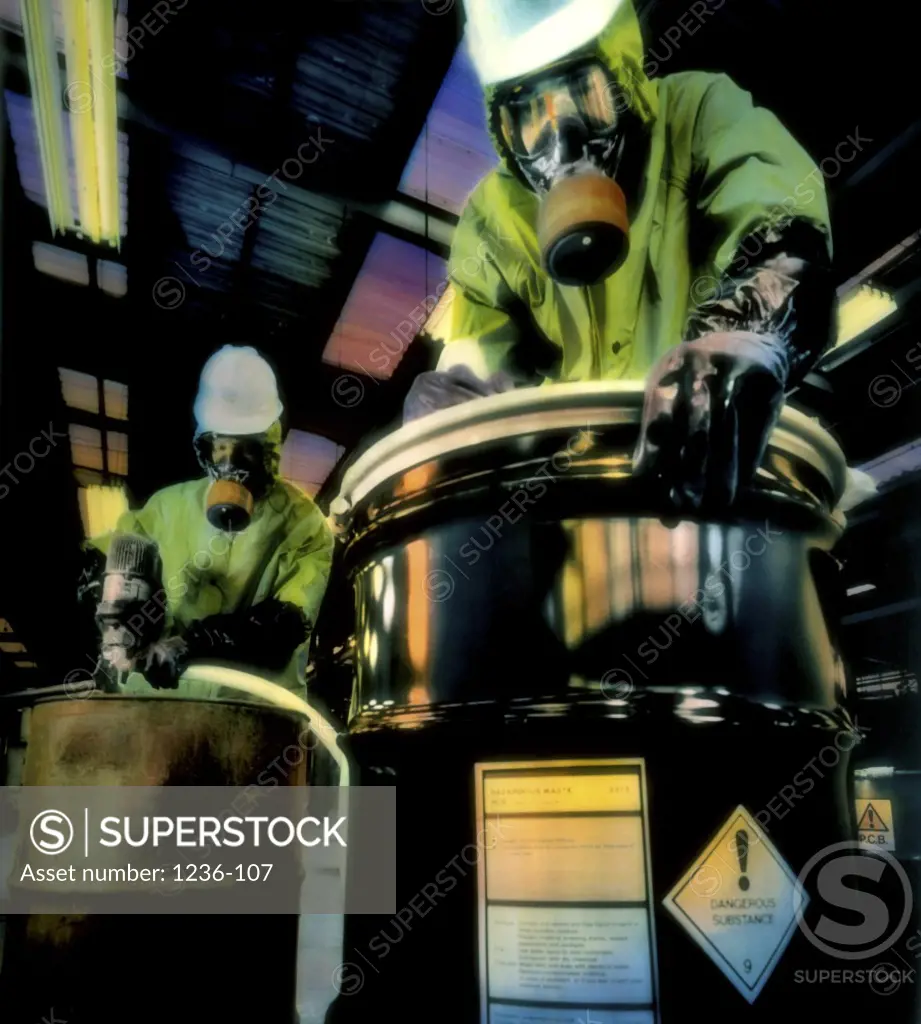 Low angle view of men wearing protective gear working with barrels of hazardous chemicals