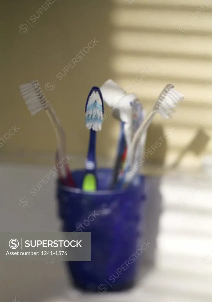 Close-up of three toothbrushes with a tube of toothpaste in a bathroom