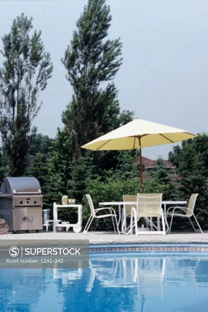Empty chairs and table under a patio umbrella at poolside