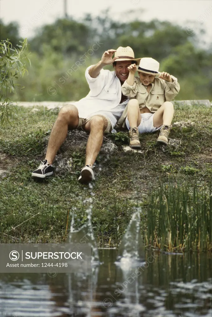 Father sitting with his son on a river bank throwing stones in the water