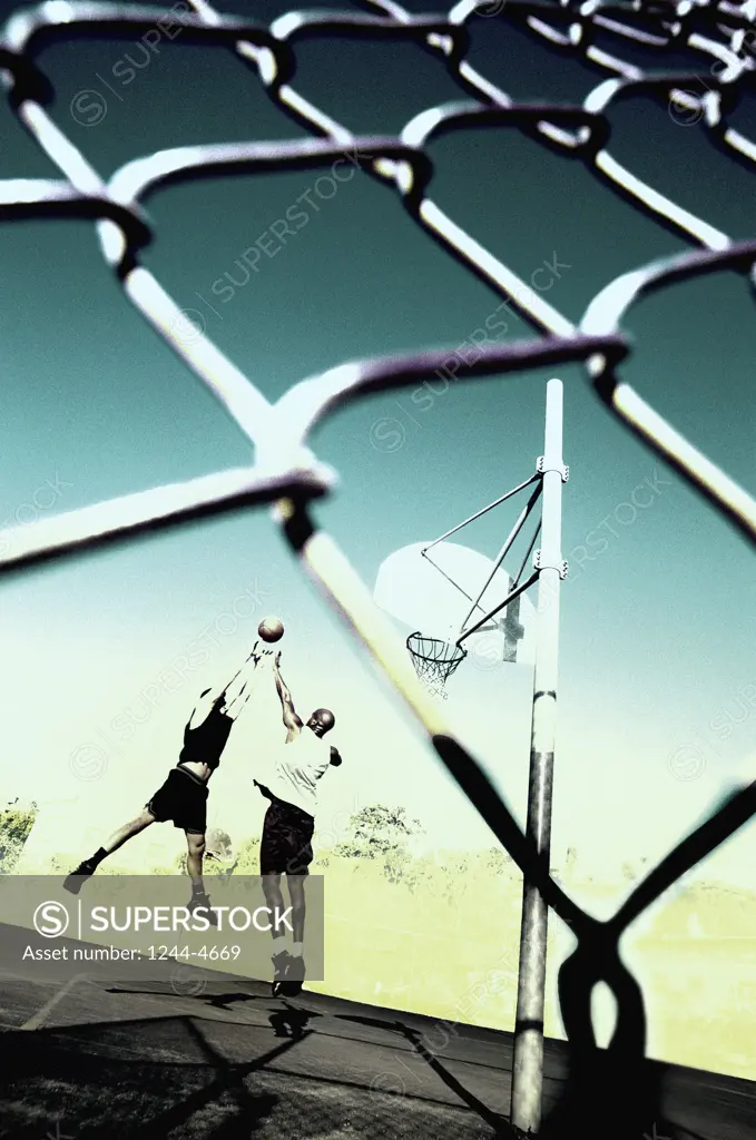 Low angle view of two men playing basketball behind a chain-link fence