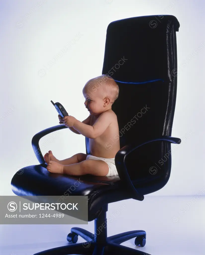 Baby sitting in an office chair and holding a mobile phone