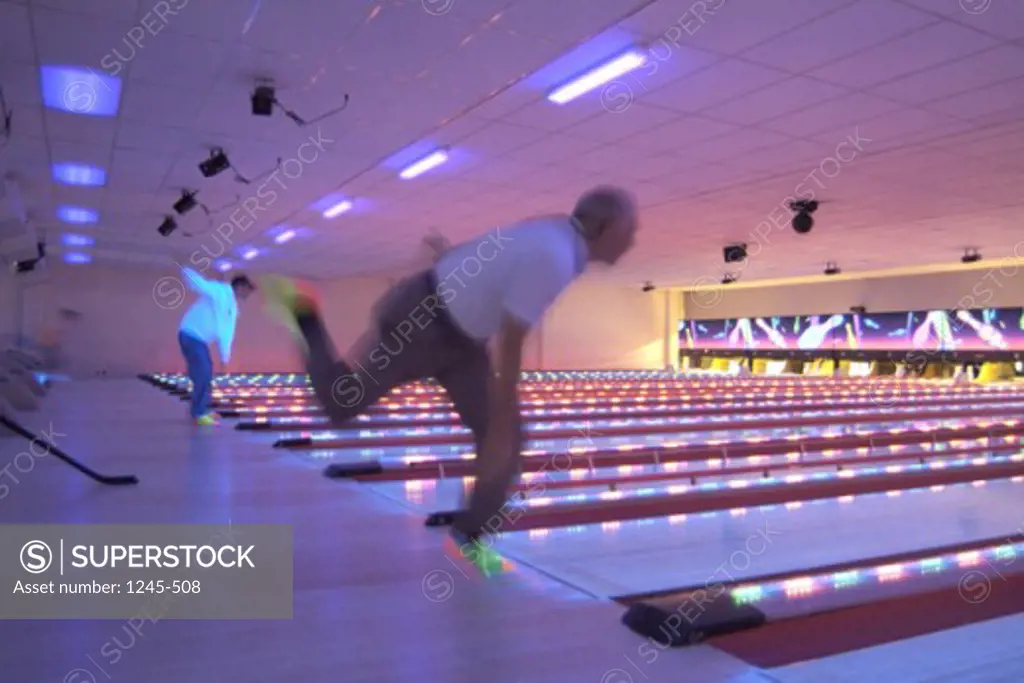Side profile of two men bowling in a bowling alley