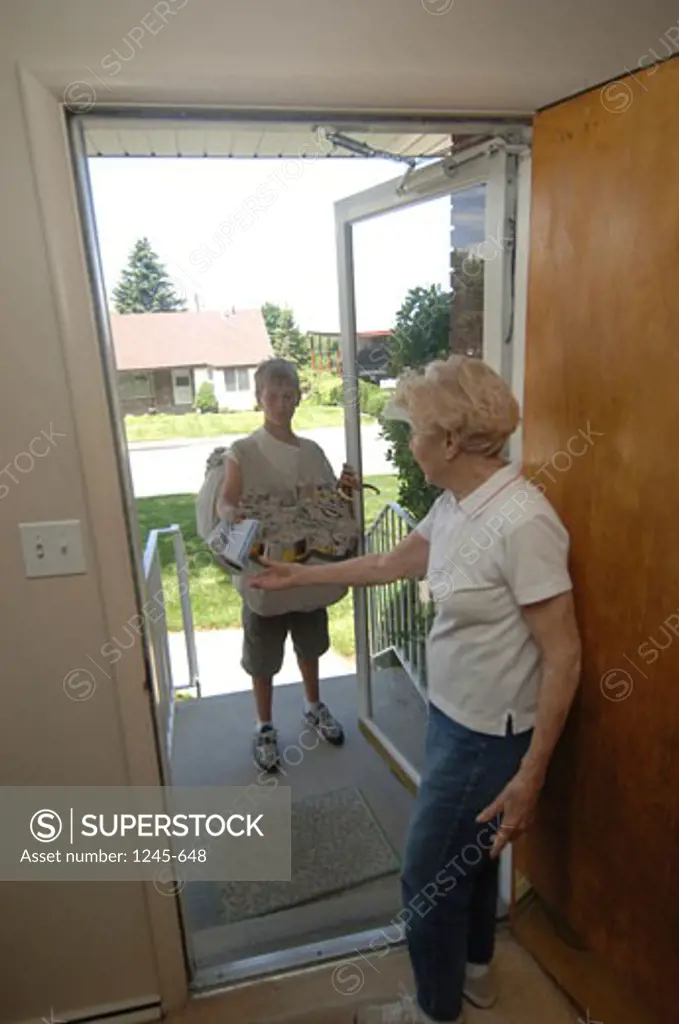Senior woman receiving a newspaper from a paper delivery boy