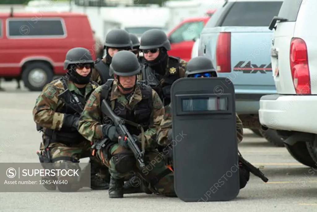 Group of SWAT team members behind a riot shield