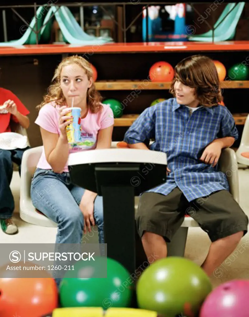 Teenage boy and a teenage girl sitting in a bowling alley