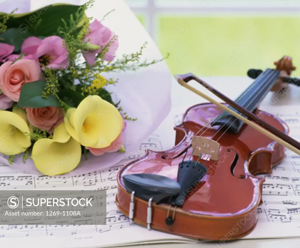Close-up of a violin and a bouquet of flowers on sheet music