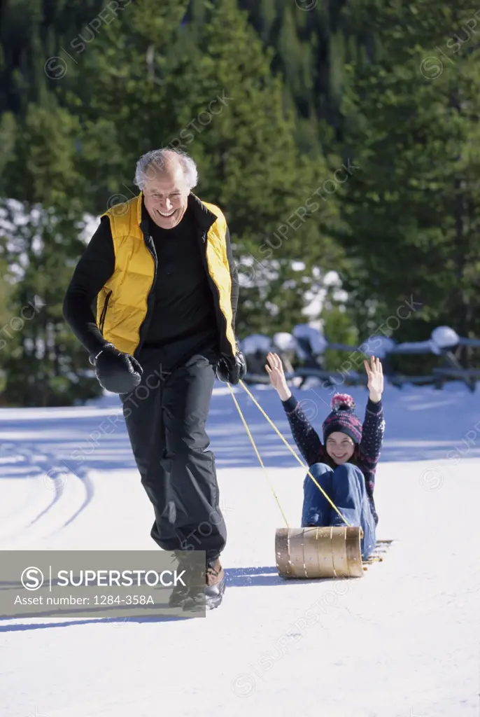 Senior man pulling his granddaughter on a sled