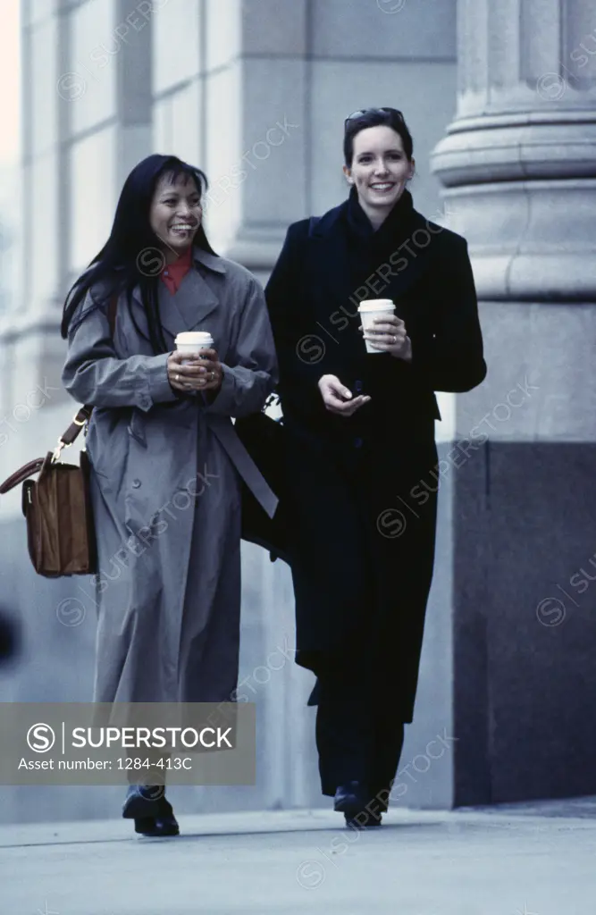 Two businesswomen holding disposable cups and smiling,