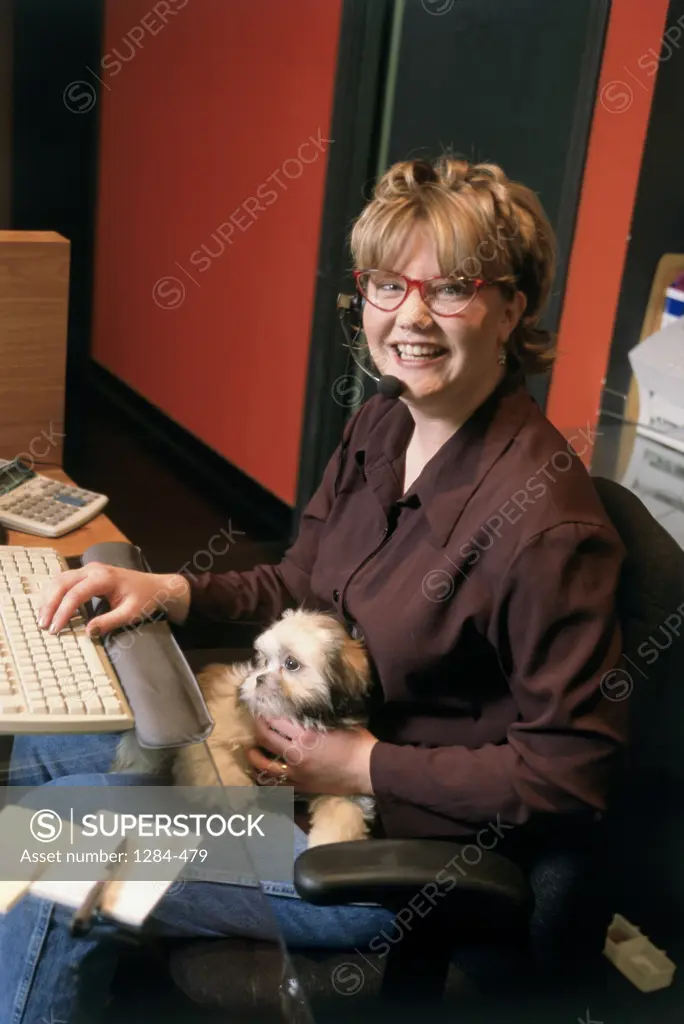 Businesswoman sitting in front of a computer keyboard with a dog on her lap