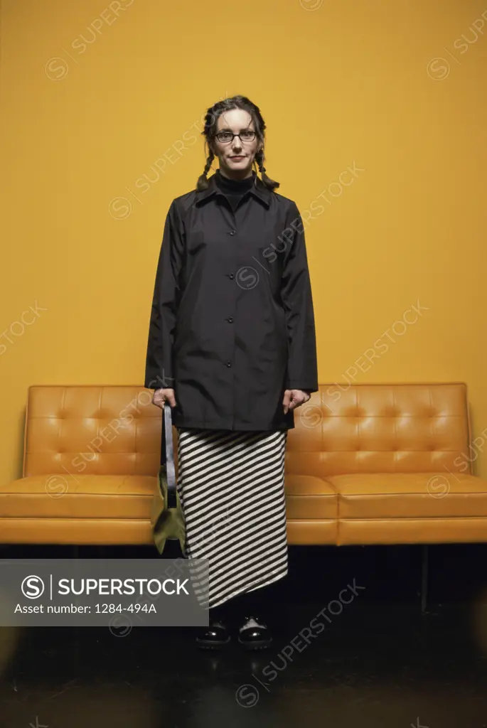 Young woman holding a handbag standing in front of an orange sofa