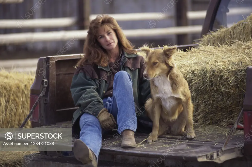 Portrait of a woman sitting at the back of a pick-up truck with her dog