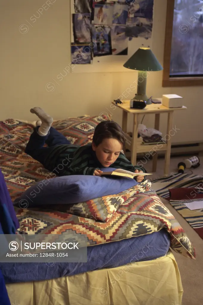 High angle view of a boy lying in bed reading