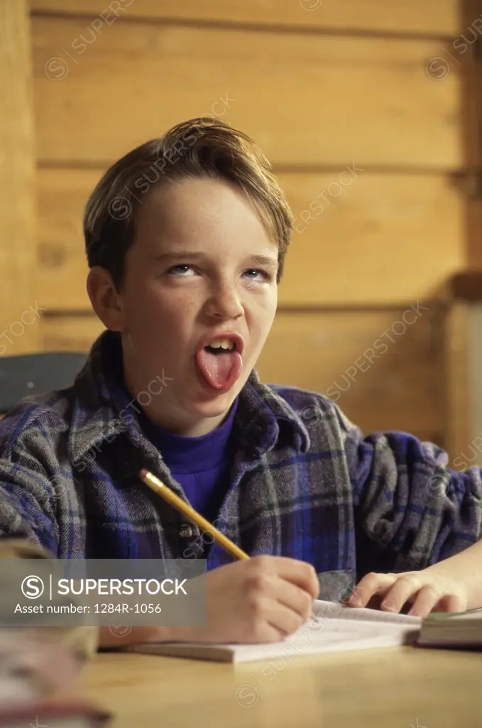 Portrait of a boy seated at a desk in front of a book making a face