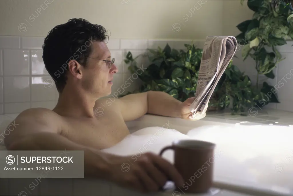 Side profile of a mid adult man sitting in a tub reading a newspaper