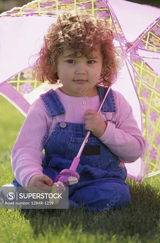 Portrait of a girl sitting on a lawn holding an umbrella