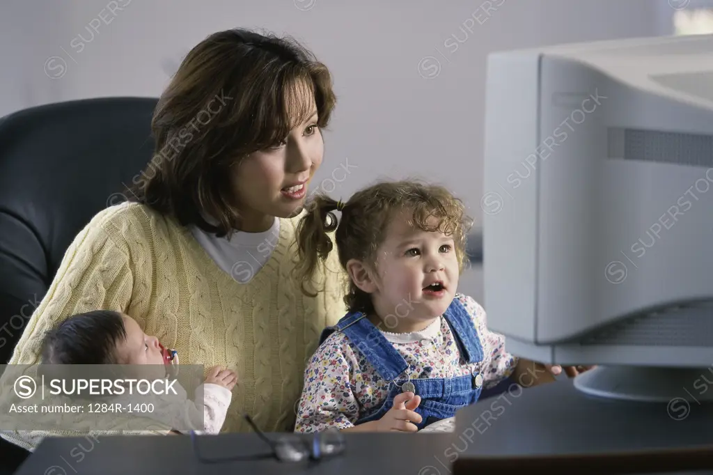 Mother sitting in front of a computer monitor with her two daughters