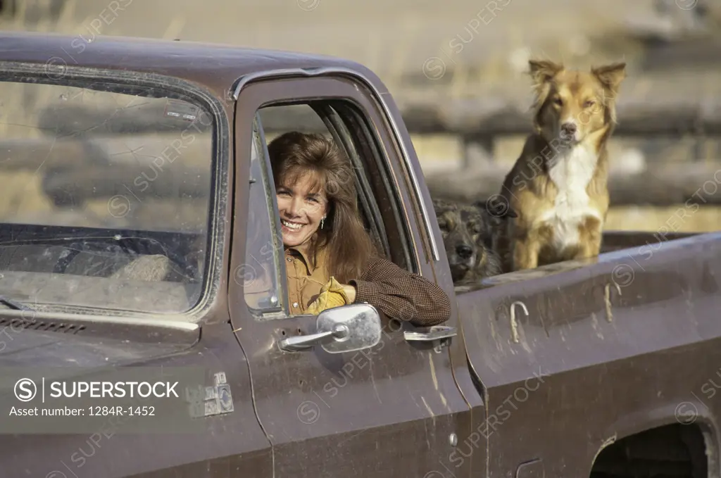 Portrait of a woman sitting in a pick-up truck with her dog behind