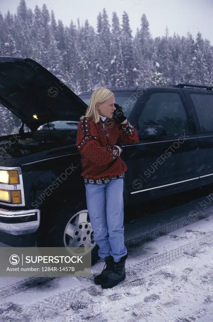 Young woman near a broken down car talking on a mobile phone