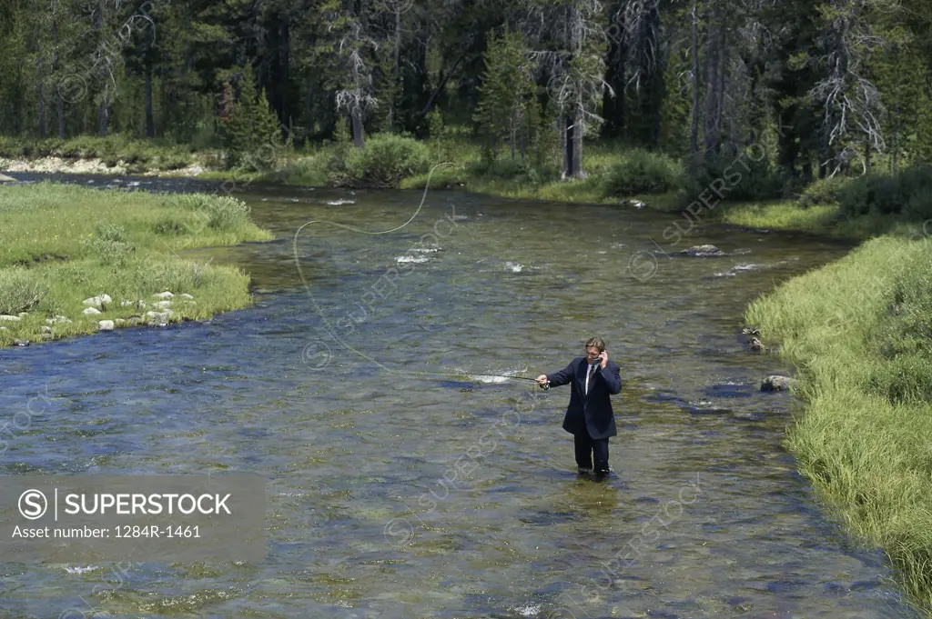 Businessman fly-fishing in a river while talking on a mobile phone