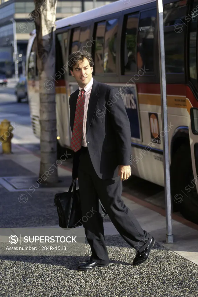 Side profile of a businessman holding a briefcase standing near a bus