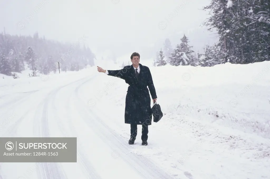 Businessman standing on a snow covered road hitchhiking