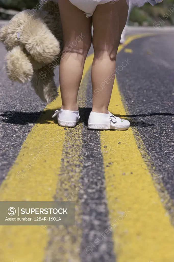 Low section view of a girl's feet standing on a road holding a stuffed toy