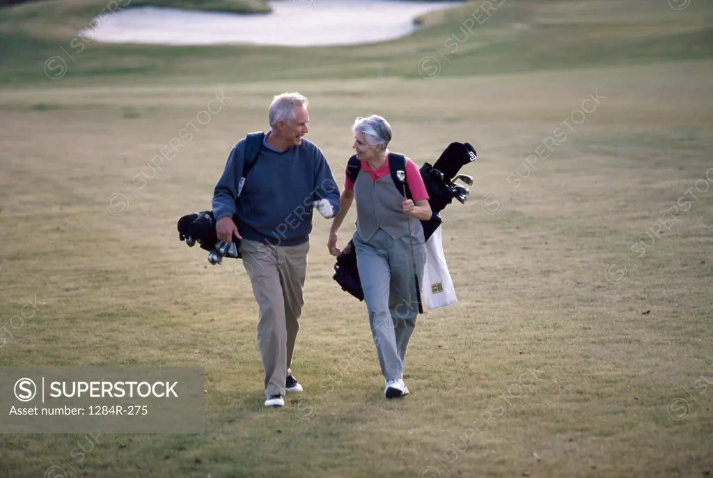 Senior couple walking on a golf course carrying golf bags