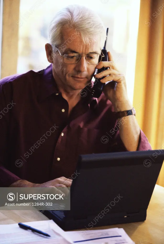 Senior man using a laptop talking on a mobile phone