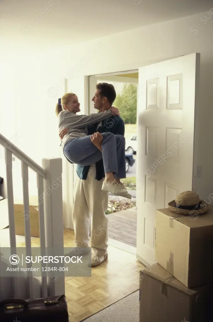 Young man carrying a young woman at the doorway of new house