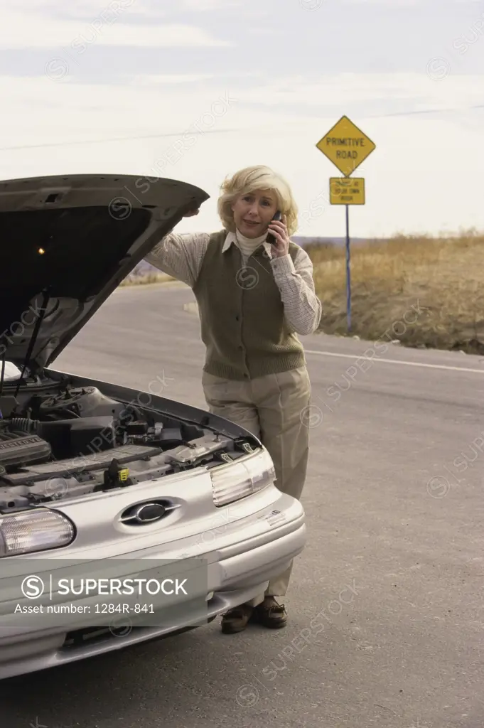 Senior woman standing near a broken down car talking on a mobile phone