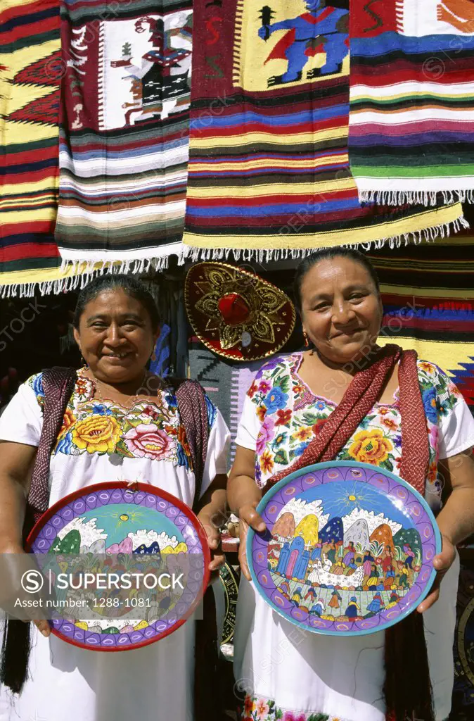 Portrait of two mature women holding decorated plates, Cancun, Mexico