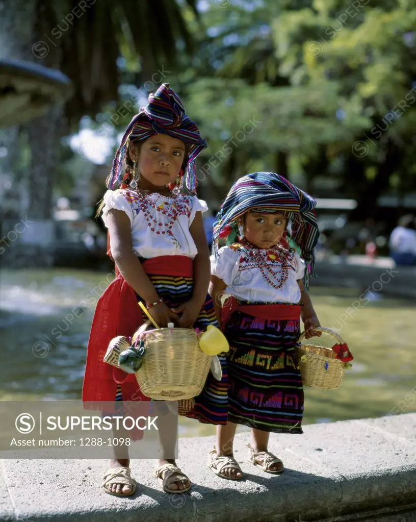 Portrait of two girls standing holding baskets, Oaxaca, Mexico