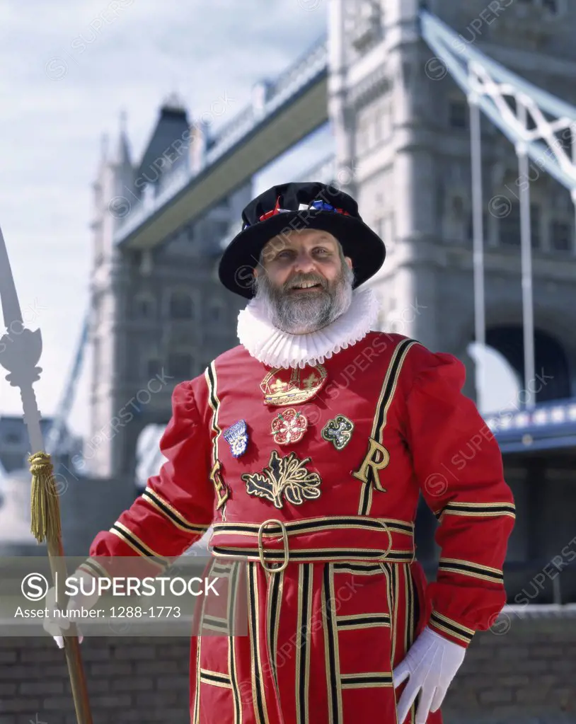 Portrait of a Beefeater standing with a bridge in the background, Tower Bridge, London, England