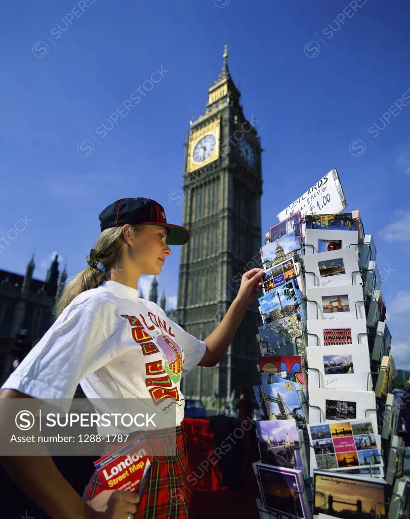 Side profile of a young woman choosing postcards with a clock tower in the background, Big Ben, London, England