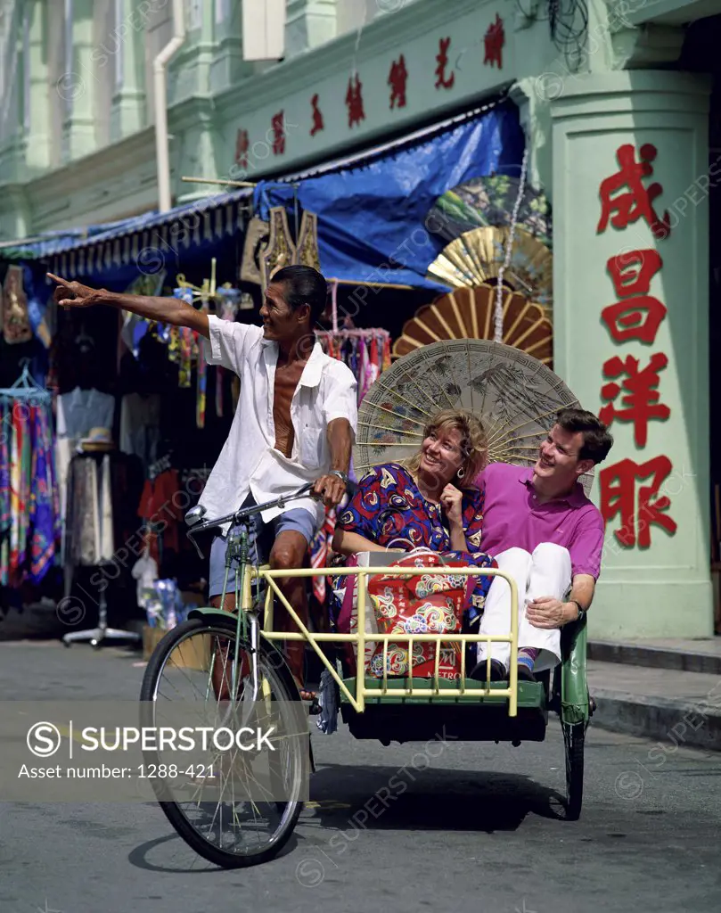 Mid adult couple traveling by rickshaw, Chinatown, Singapore