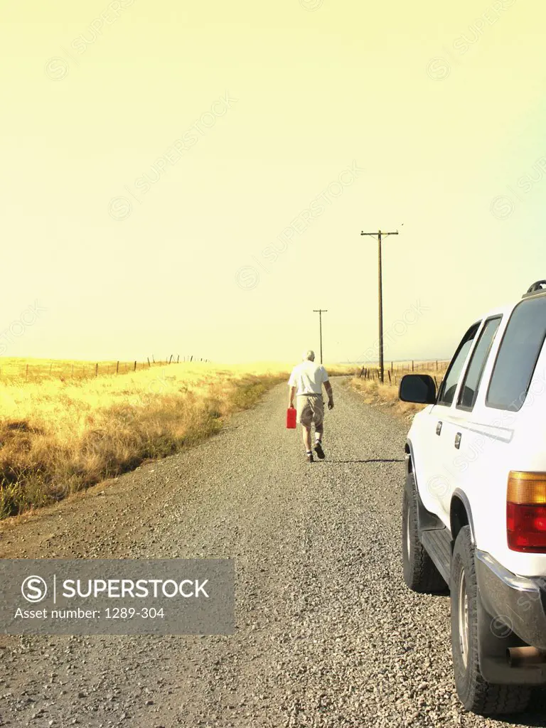 Senior man walking down a road holding a petrol container