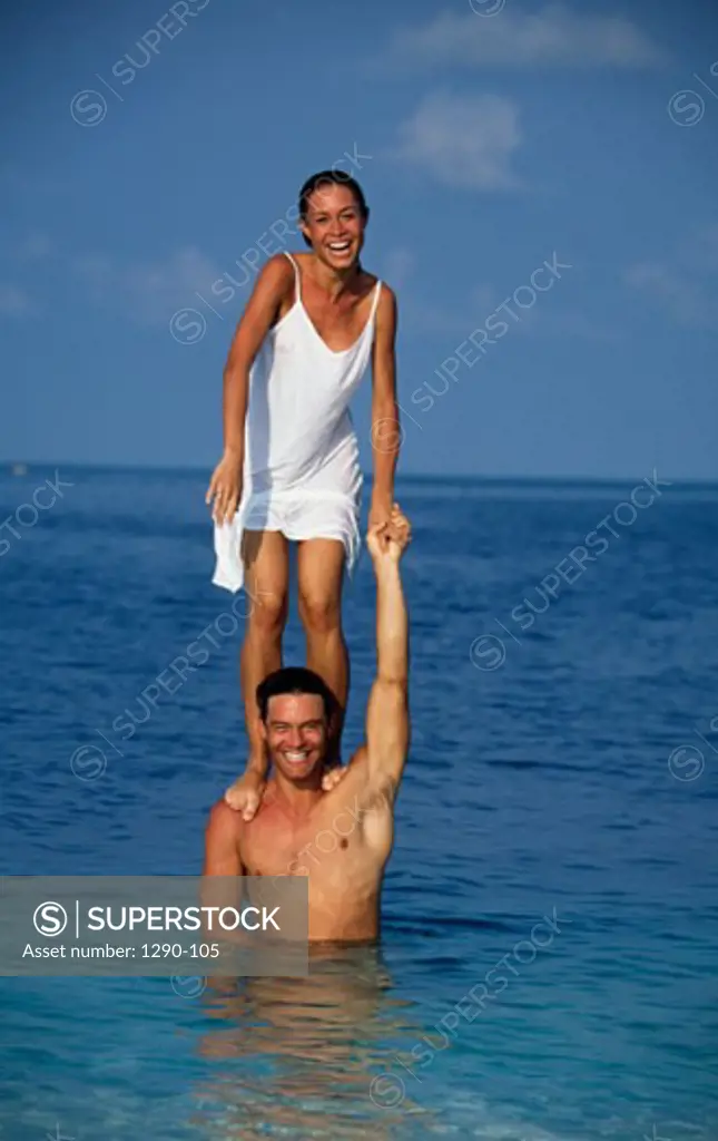 Portrait of a young woman standing on the shoulders of a young man in the ocean