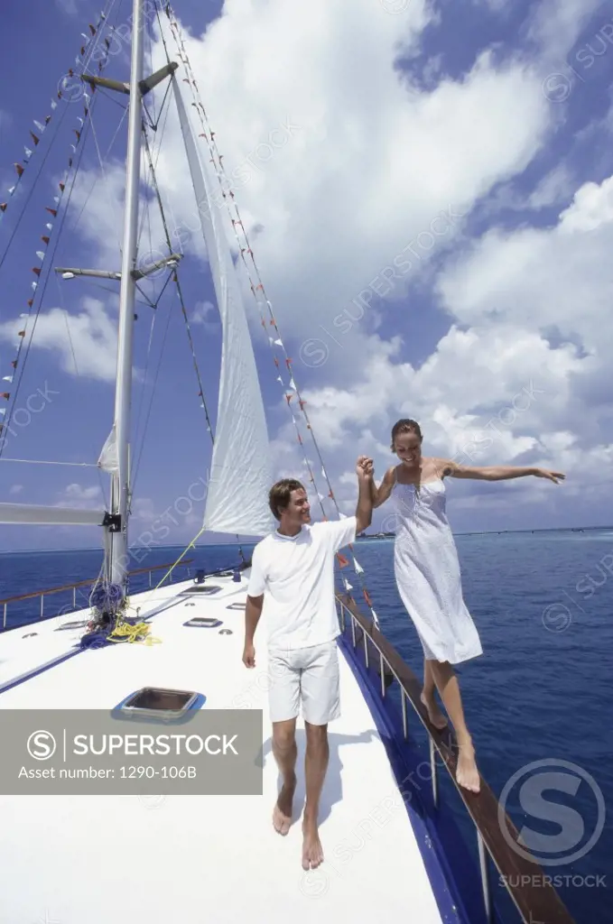 Young woman walking on a railing of a sailboat with a young man holding her hand