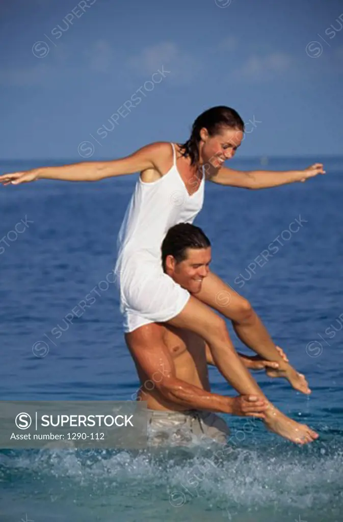 Young man standing in water carrying a young woman on his shoulders